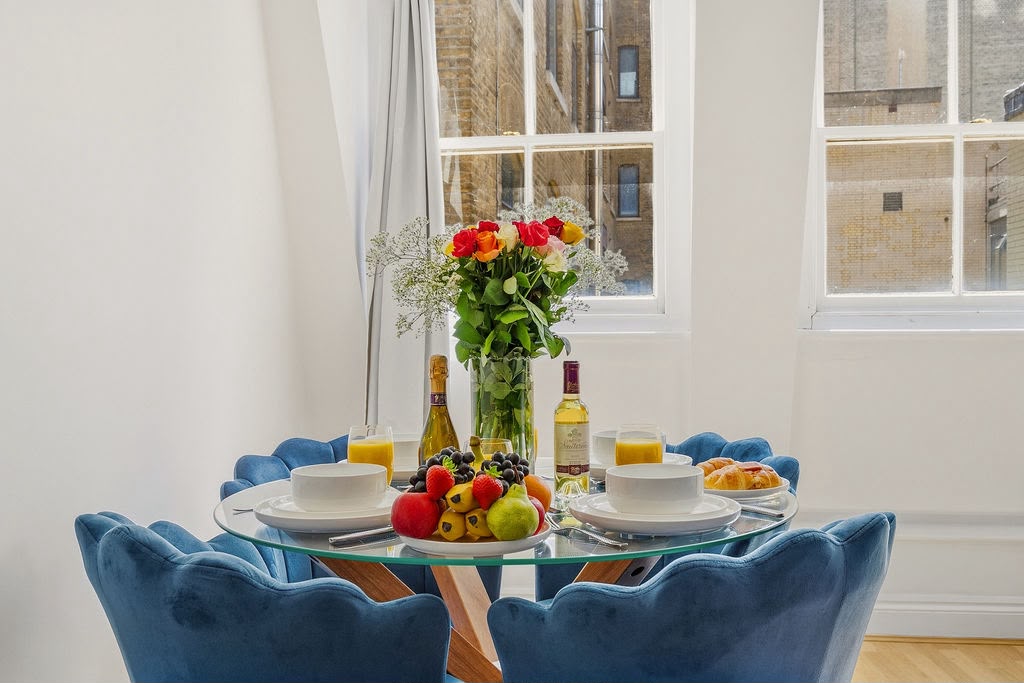 Glass dining table set for breakfast beside tall windows