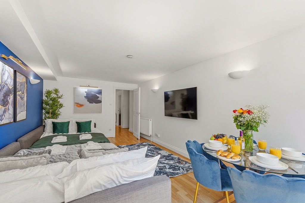 Wide view of the living space with beds, wall-mounted TV and dining area